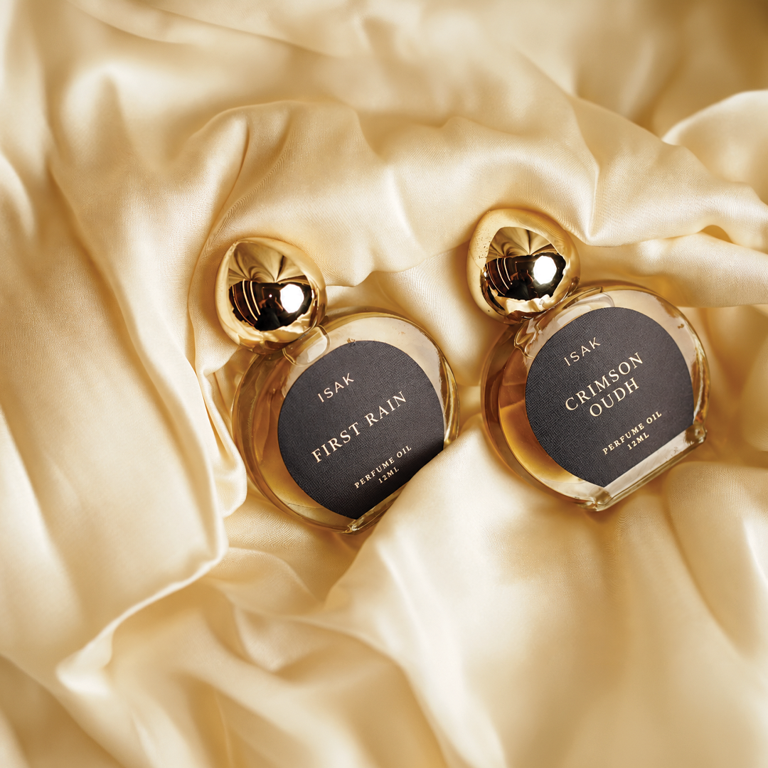 Two gold cap attar bottles with oval labels: First Rain and Crimson Oudh on satin