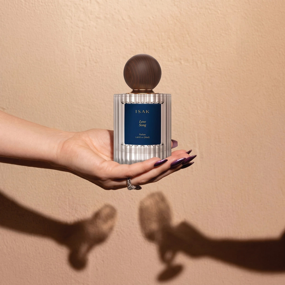 ISAK perfume bottle held in hand, dark round cap on silver ribbed glass.
