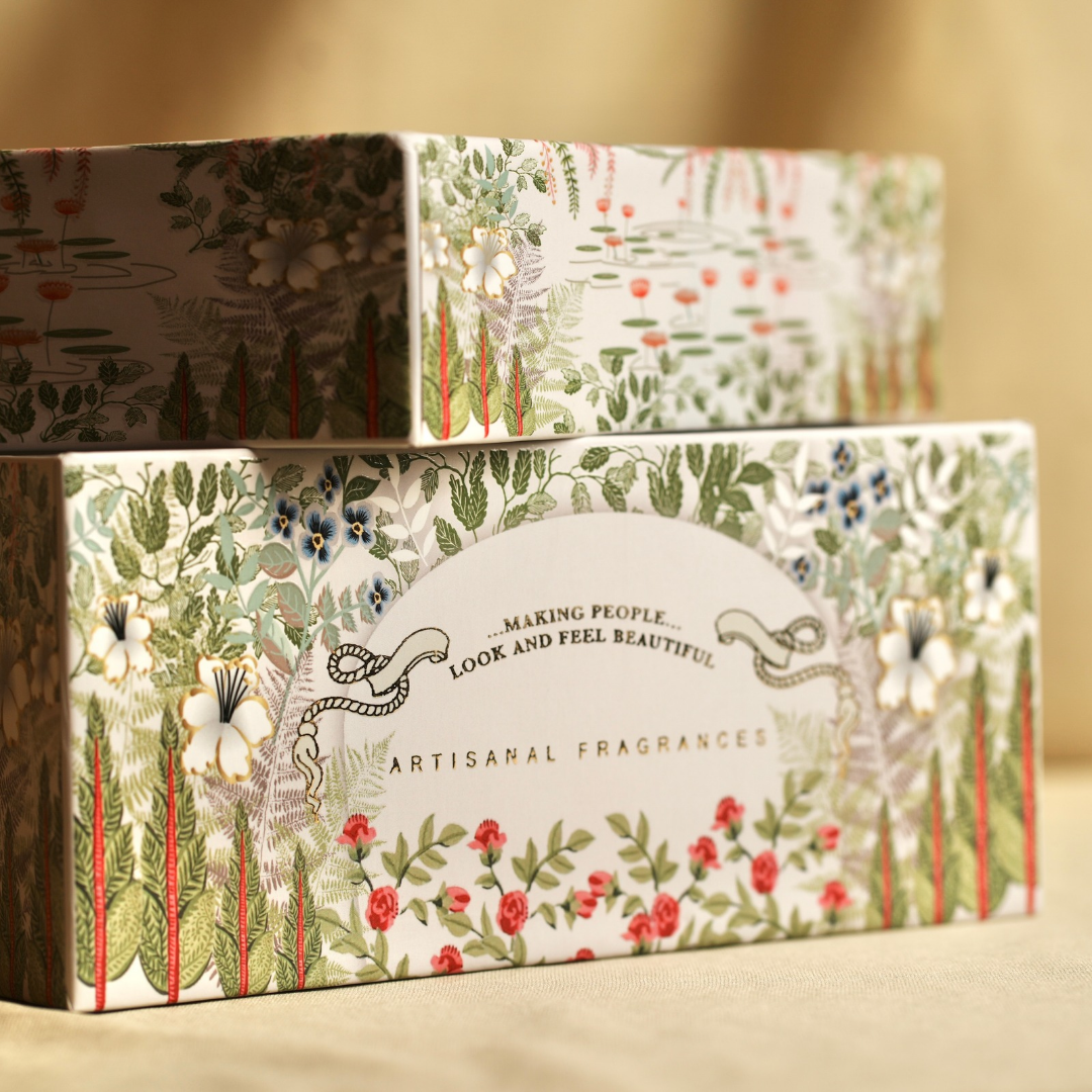 Stacked gift boxes with floral scenes and "ARTISANAL FRAGRANCES" text on sides